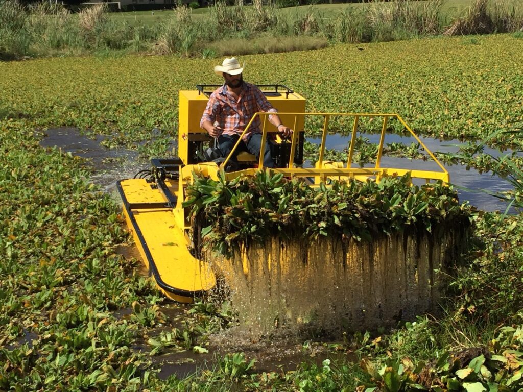 Man operating yellow aquatic weed harvester