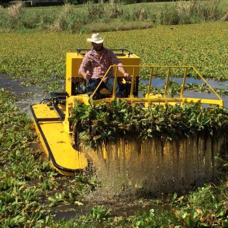 Man operating yellow aquatic weed harvester